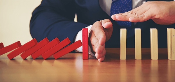 a man prevents a row of falling dominoes from knocking over the dominoes still standing