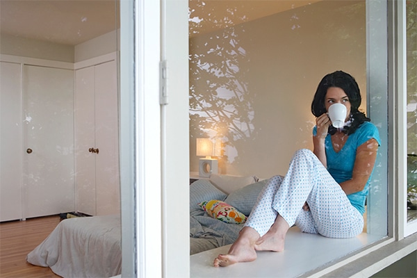 a woman drinking coffee looks out her bedroom window