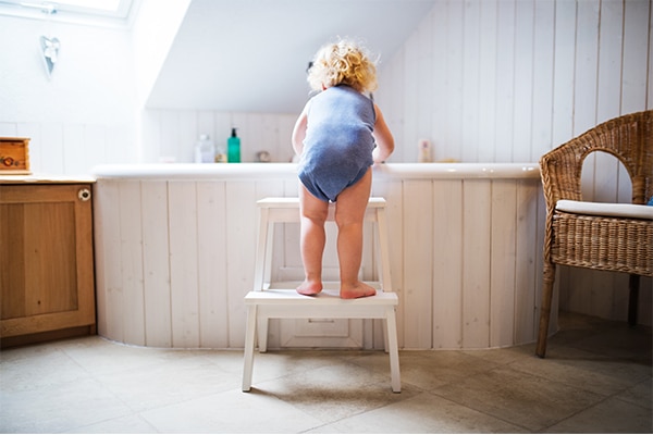 a child standing on a stool in a bathroom
