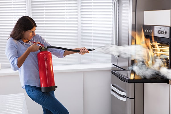 a woman using a fire extinguisher to put out an oven fire